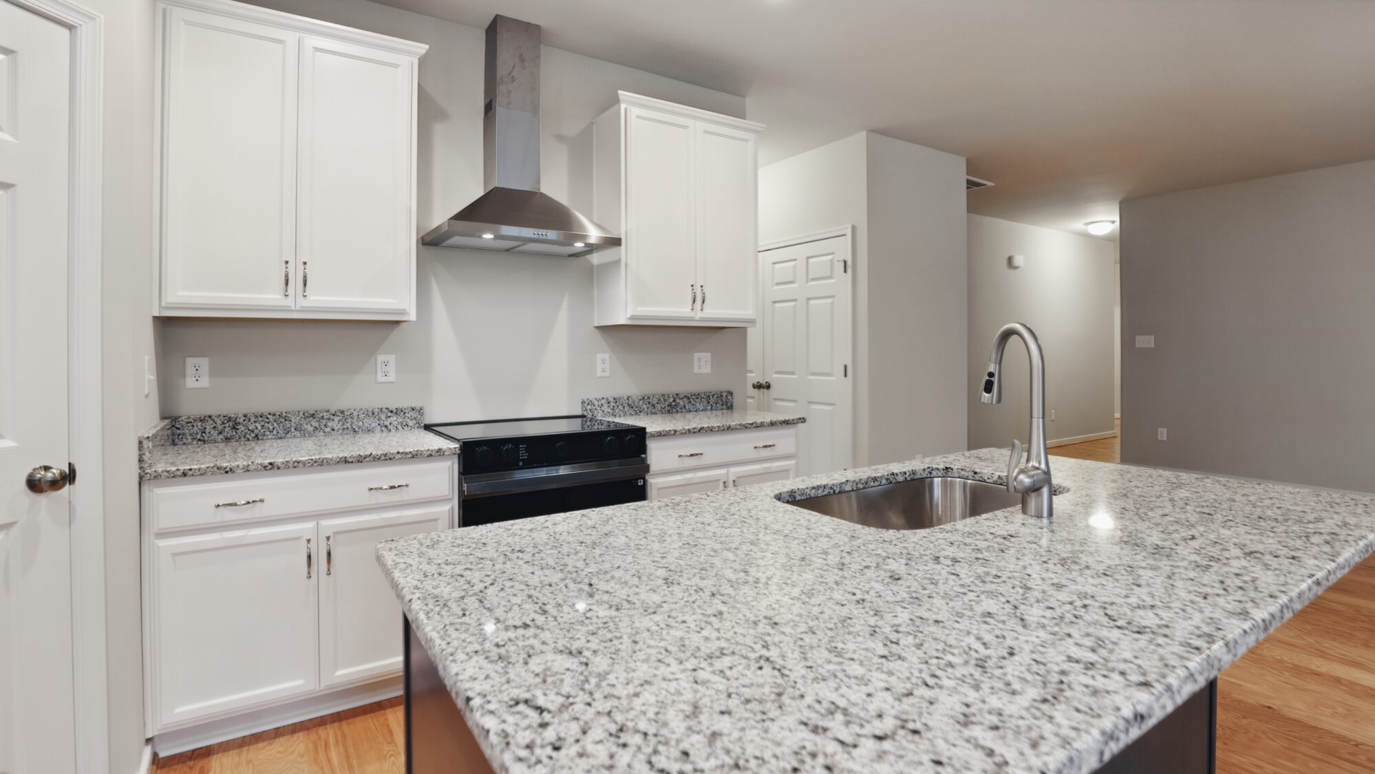Modern Somerset Hill kitchen with white cabinets, stainless appliances, and a granite island with a sink.