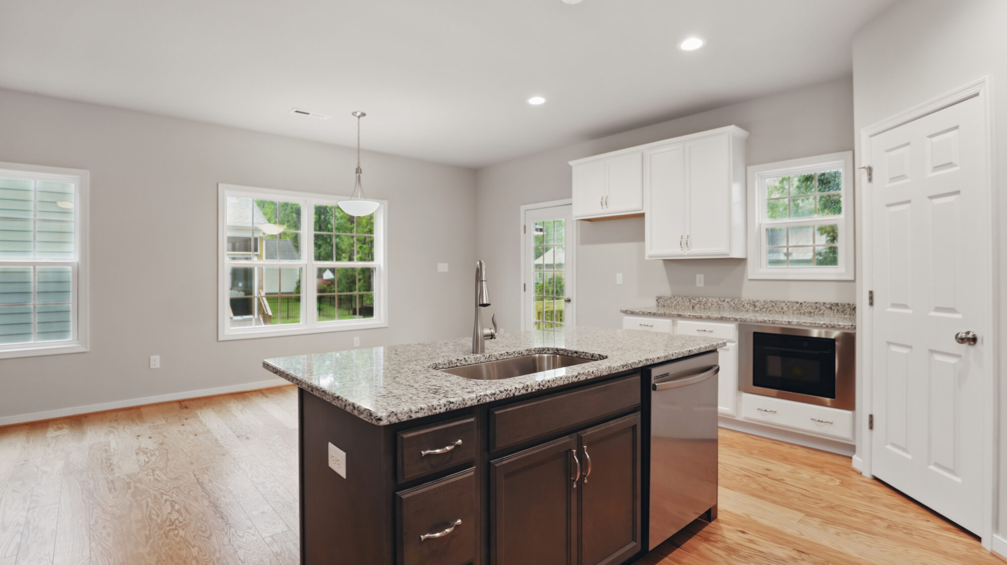 Modern Somerset Hill kitchen with granite island, stainless appliances, white cabinets, and hardwood floors facing dining area.