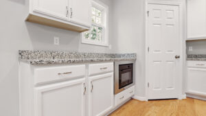 Modern Bethany kitchen with white cabinets, granite countertop, stainless oven, and light wood flooring.