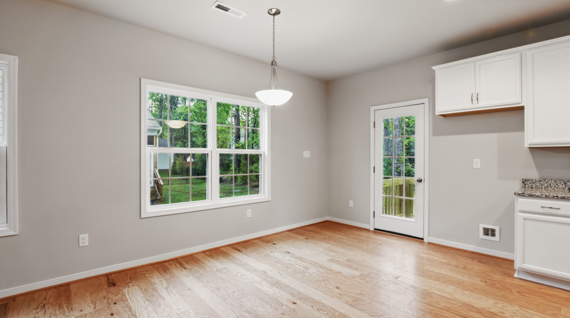 Bright, empty kitchen with wood floors, white cabinets, and a large window in desirable Somerset Hill.