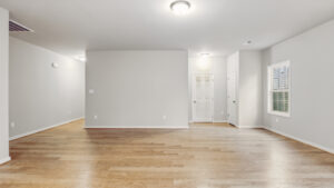 Spacious empty room in Bethany's Somerset Hill, with light wood floors, gray walls, and white doors with ceiling lights.