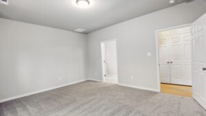 Empty room at Somerset Hill with light gray walls, gray carpet, ceiling light, and open doors to other rooms.