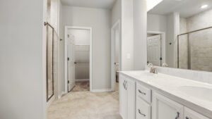 Modern Bethany bathroom with double sinks, white cabinets, glass shower, and a walk-in closet with open door.