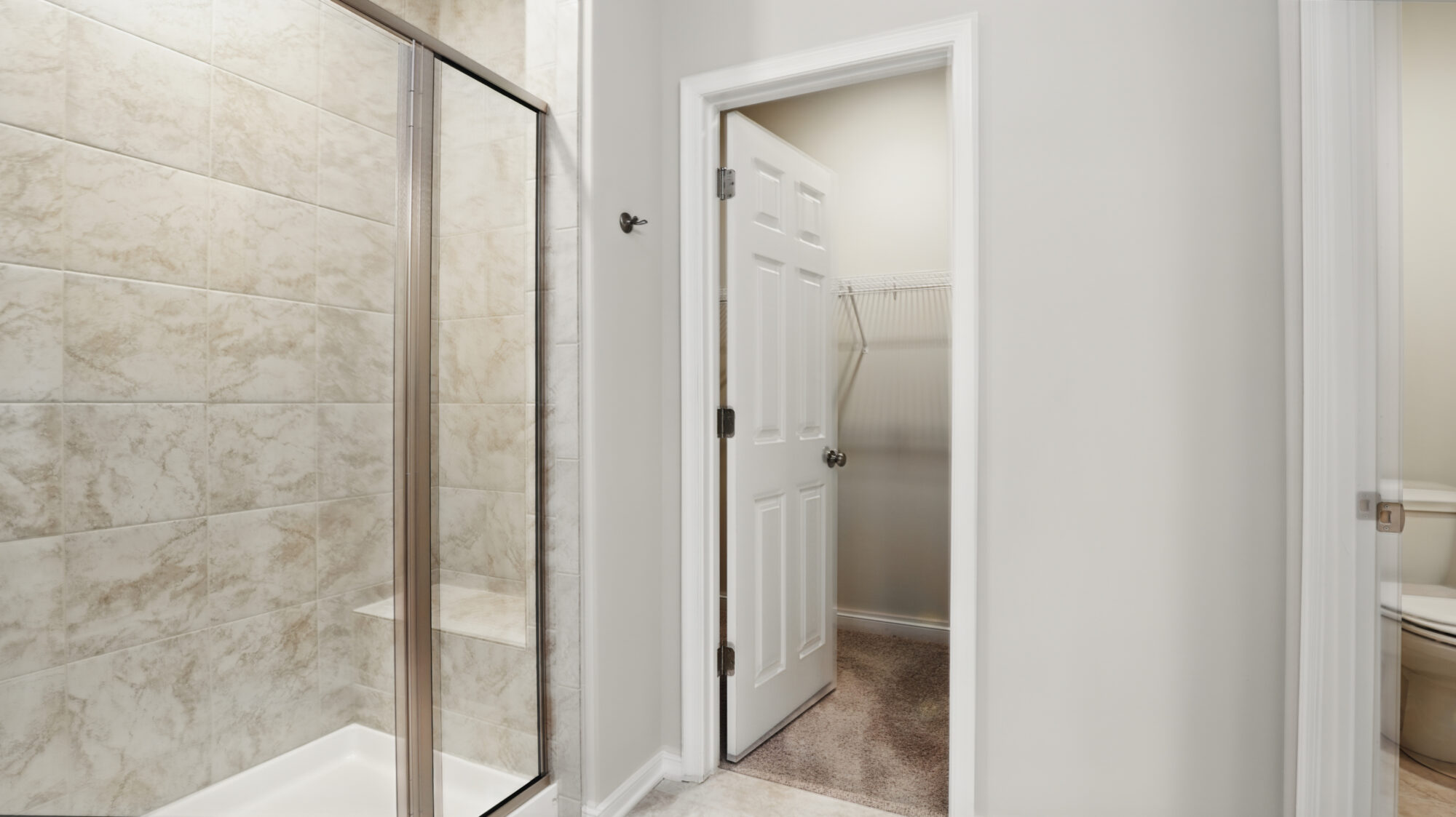Walk-in shower with glass door in Somerset Hill, next to an open door leading to a carpeted Bethany closet with wire shelves.