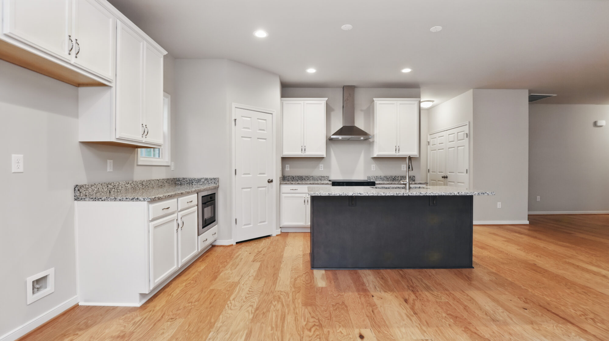 Modern Somerset Hill kitchen with white cabinets, granite counters, island, and hardwood floors in open-plan Bethany space.