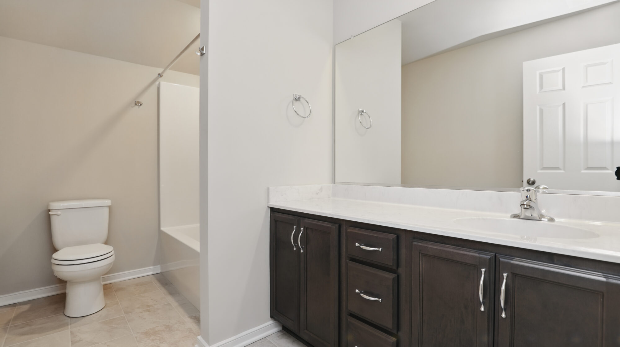 Modern Somerset Hill bathroom with dark cabinets, white countertop, toilet, and glass-door shower.
