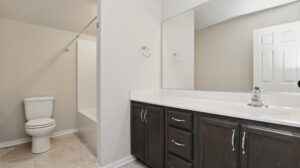 Modern Somerset Hill bathroom with dark cabinets, white countertop, toilet, and glass-door shower.