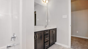 Modern bathroom at Somerset Hill with a dark wood vanity, large mirror, marble countertop, and light gray walls.