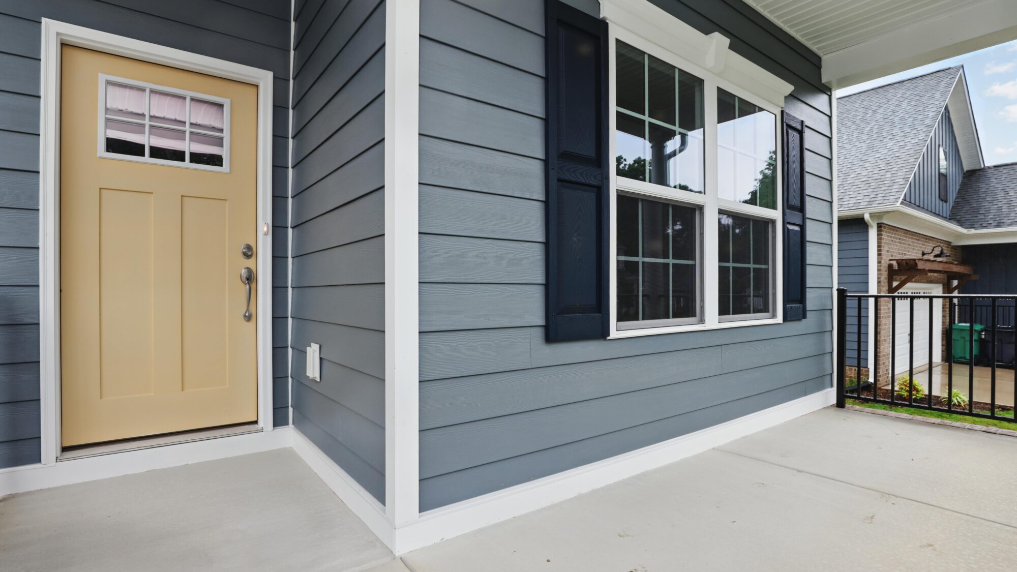 Front porch of a Somerset Hill house with blue siding, beige door, black shutters, and large windows.