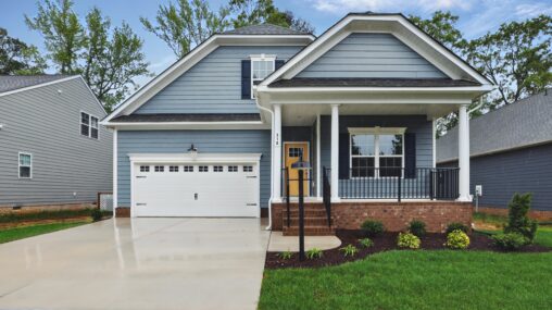 Charming blue single-story home with white trim in Somerset Hill, featuring a porch, garage, and landscaped yard.
