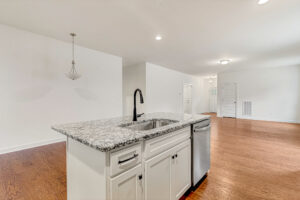 Modern kitchen at Somerset Hill with white cabinets, granite island, stainless sink, and hardwood floors.