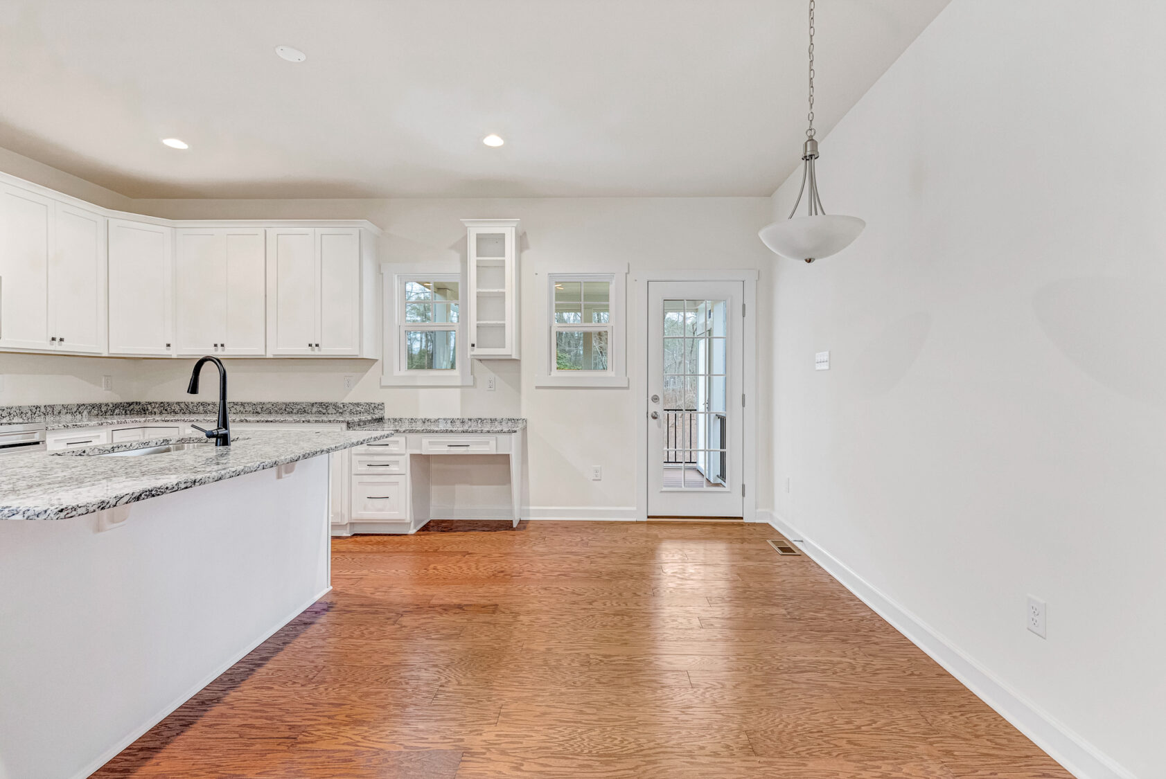 Modern kitchen with white cabinets, granite countertops, and wood floor in Somerset Hill; Kate's favorite space.