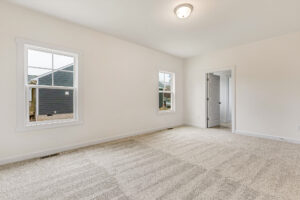 Bright empty room with beige carpet, white walls, two windows, and a door—ideal for Somerset Hill living.