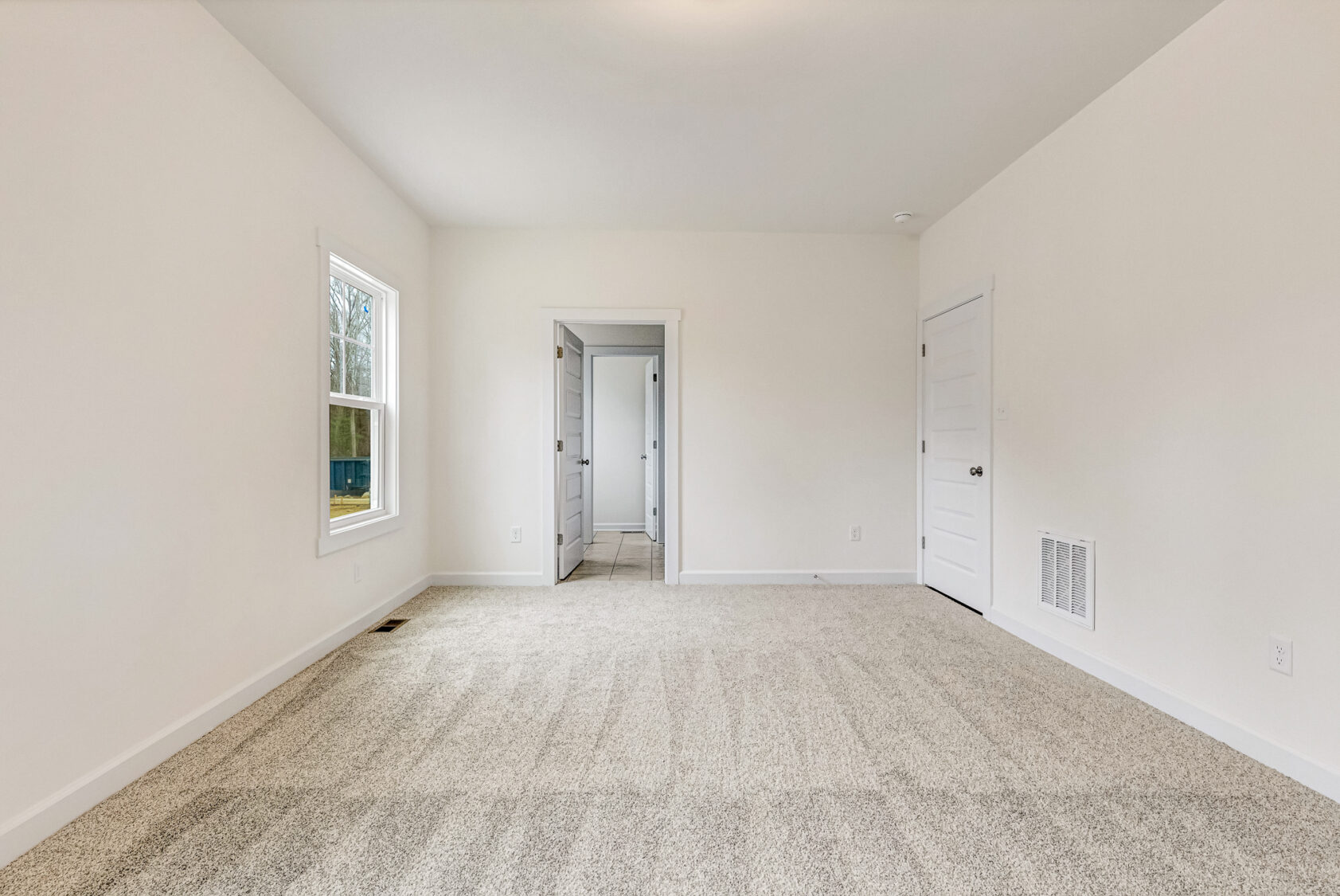 Empty, carpeted room with white walls in Somerset Hill; features a window and two white doors, one to the bathroom.