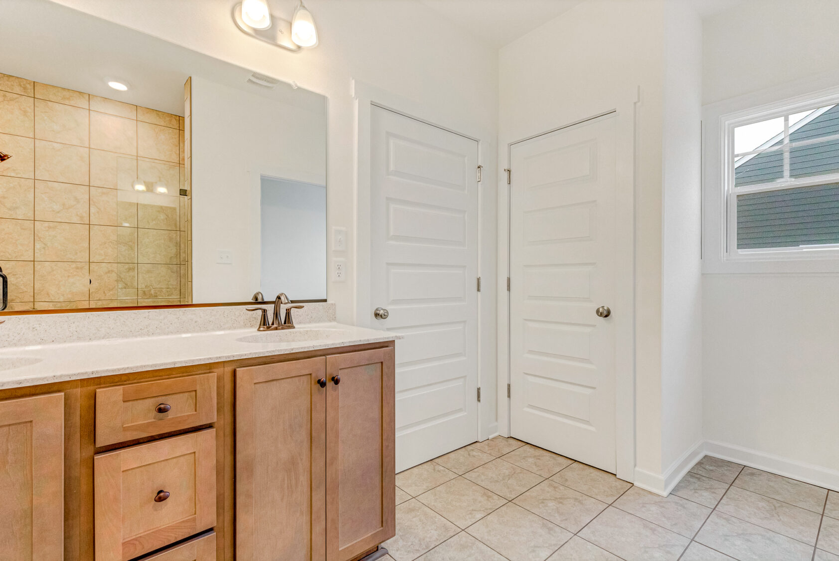 Bathroom with wooden vanity, large mirror, tiled floor, and a window on the right at Somerset Hill.
