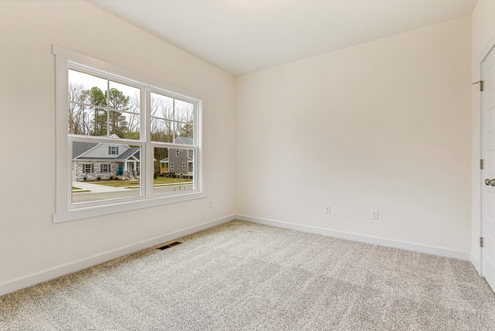 Empty room at Somerset Hill with light walls, carpeted floor, and a window overlooking houses and trees.