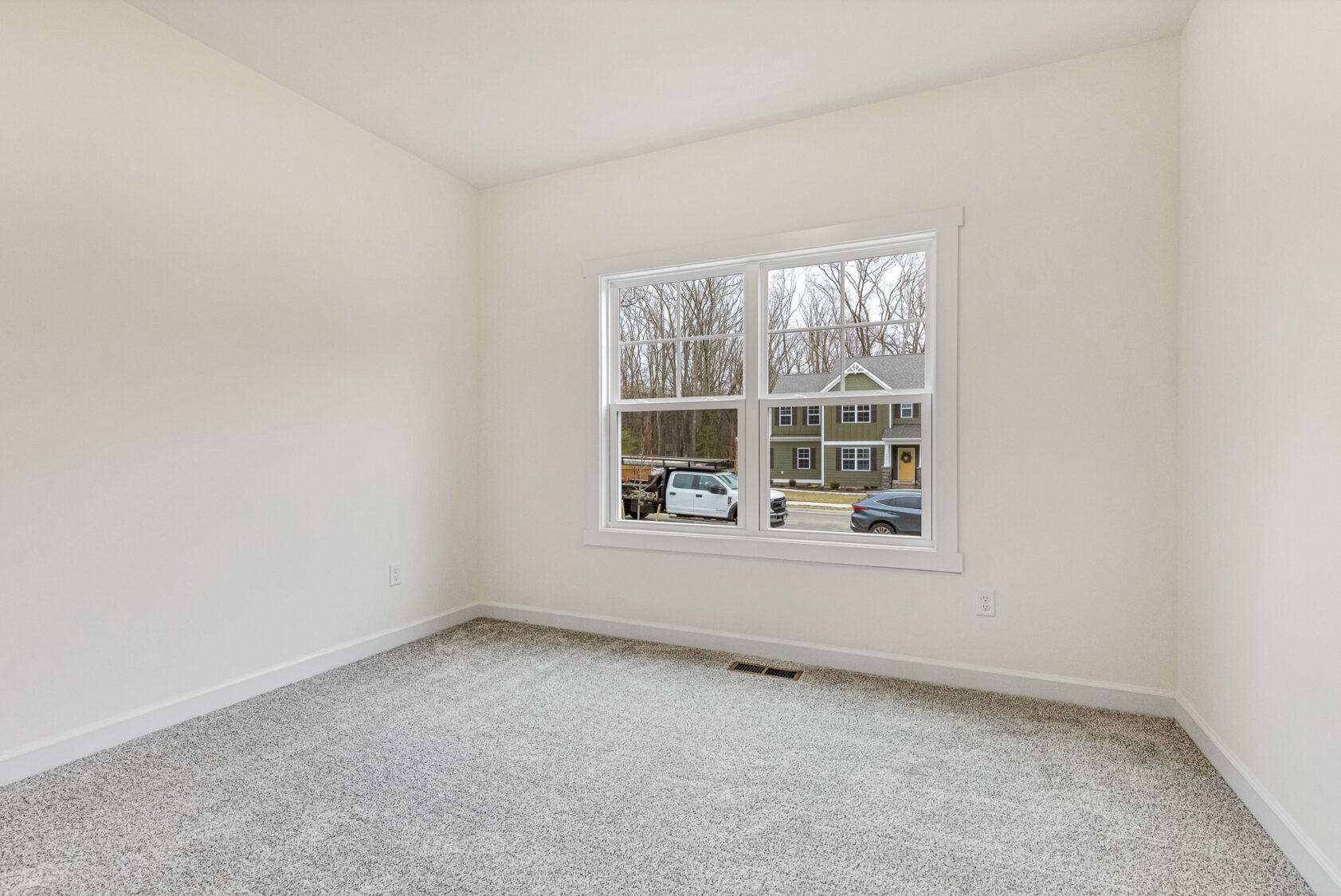 Bright empty room in Somerset Hill with beige carpet, white walls, and a window overlooking cars and houses.