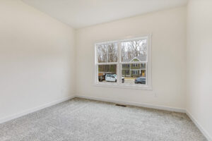 Bright empty room in Somerset Hill with beige carpet, white walls, and a window overlooking cars and houses.