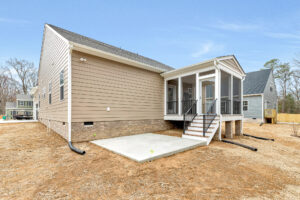 Back view of a Somerset Hill house with screened-in porch, steps, concrete patio, and brown siding on a dirt yard.
