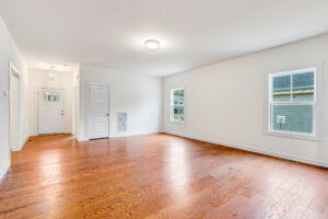 Bright, empty Somerset Hill living room with hardwood floors, white walls, and windows letting in natural light.