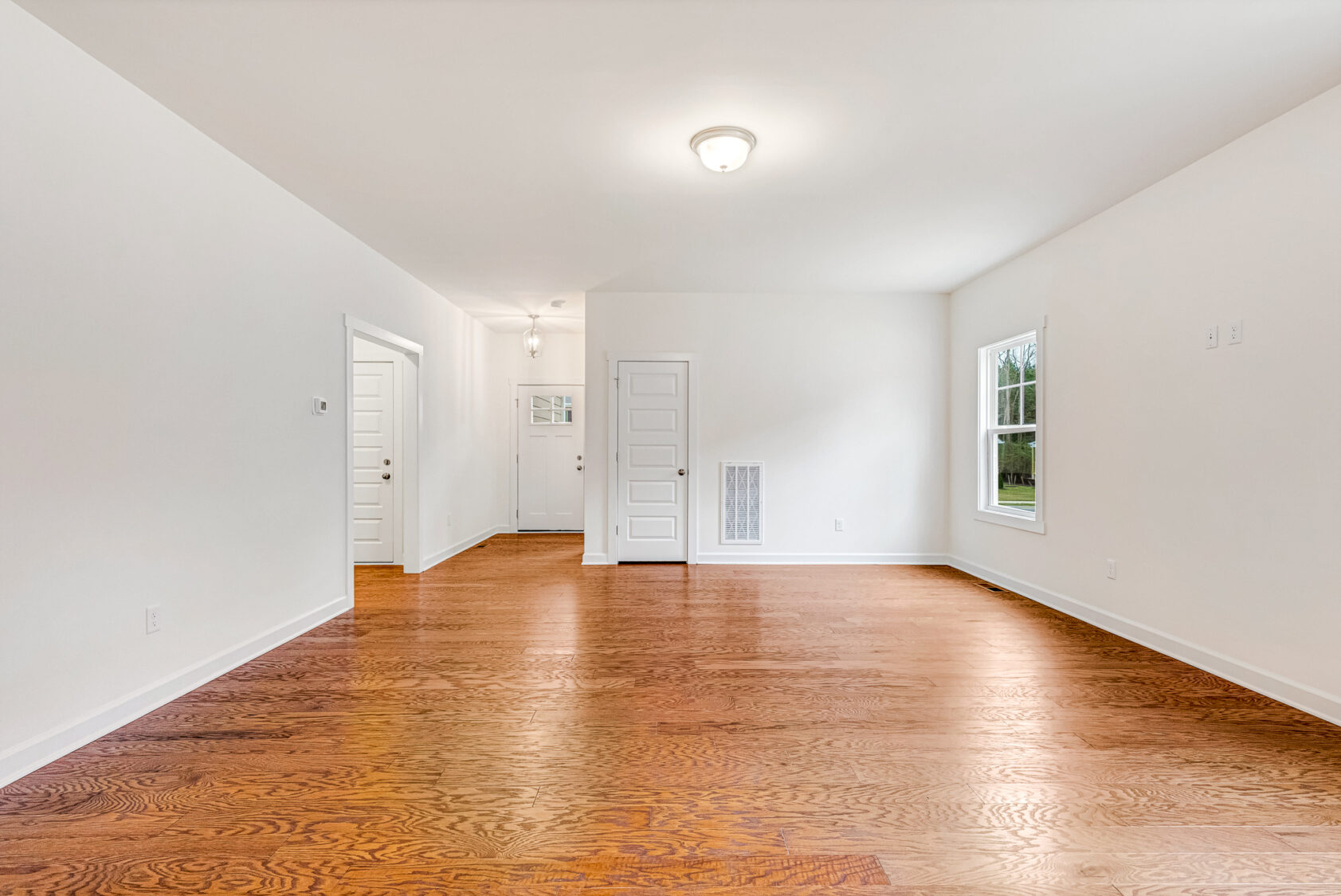 Bright, empty room at Somerset Hill with wood floors, white walls, ceiling light, and a window letting in natural light.