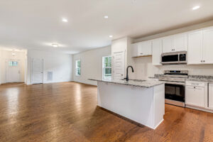 Spacious open kitchen and living area at Somerset Hill with wood floors, white cabinets, and stainless steel appliances.