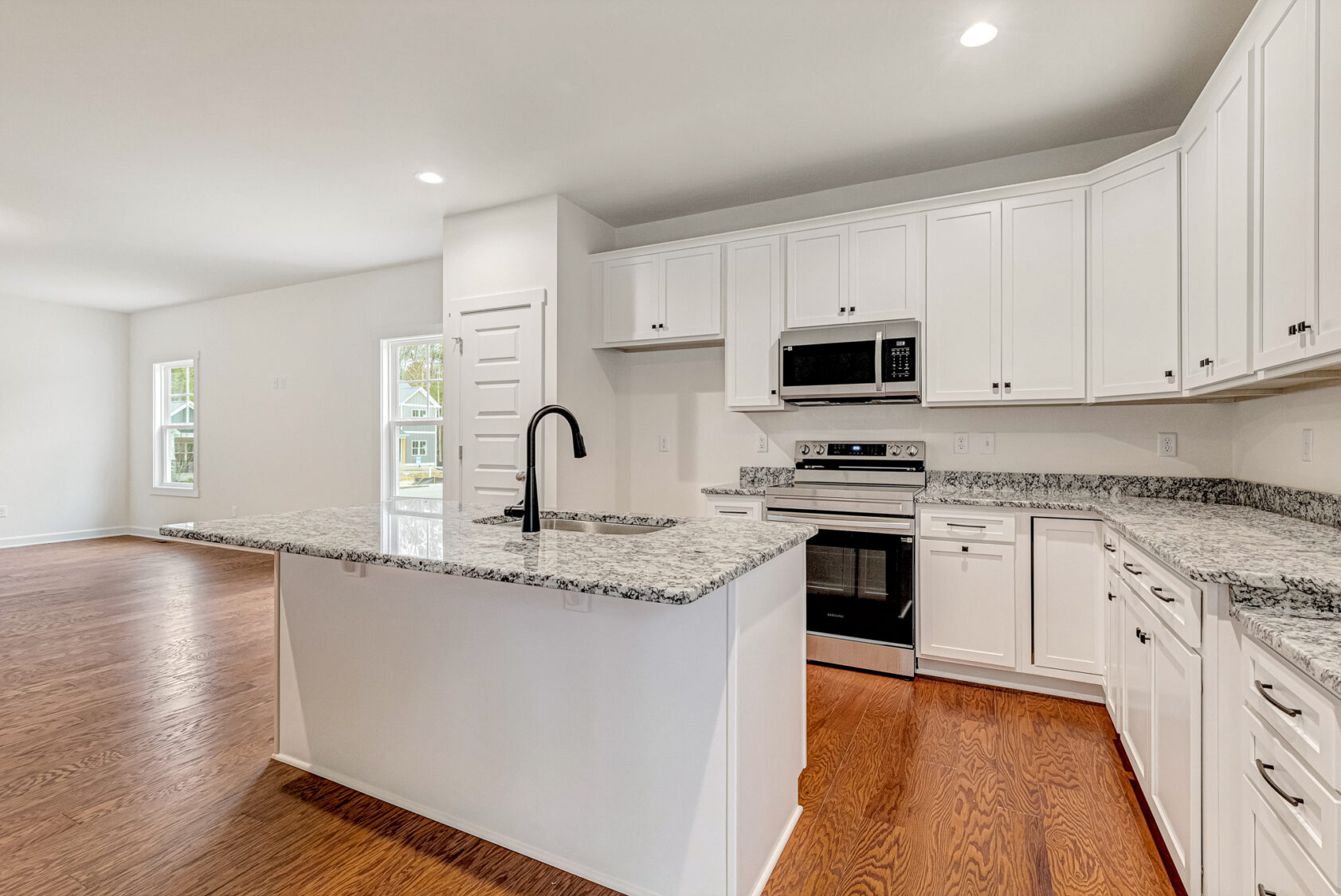 Modern Somerset Hill kitchen with white cabinets, granite counters, island, stainless appliances, and wooden floors.