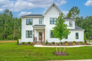Modern white two-story house in Poplar Village with large windows, front porch, and green lawn with a young tree.