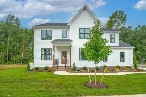 Modern white two-story house in Poplar Village with large windows, front porch, and green lawn with a young tree.