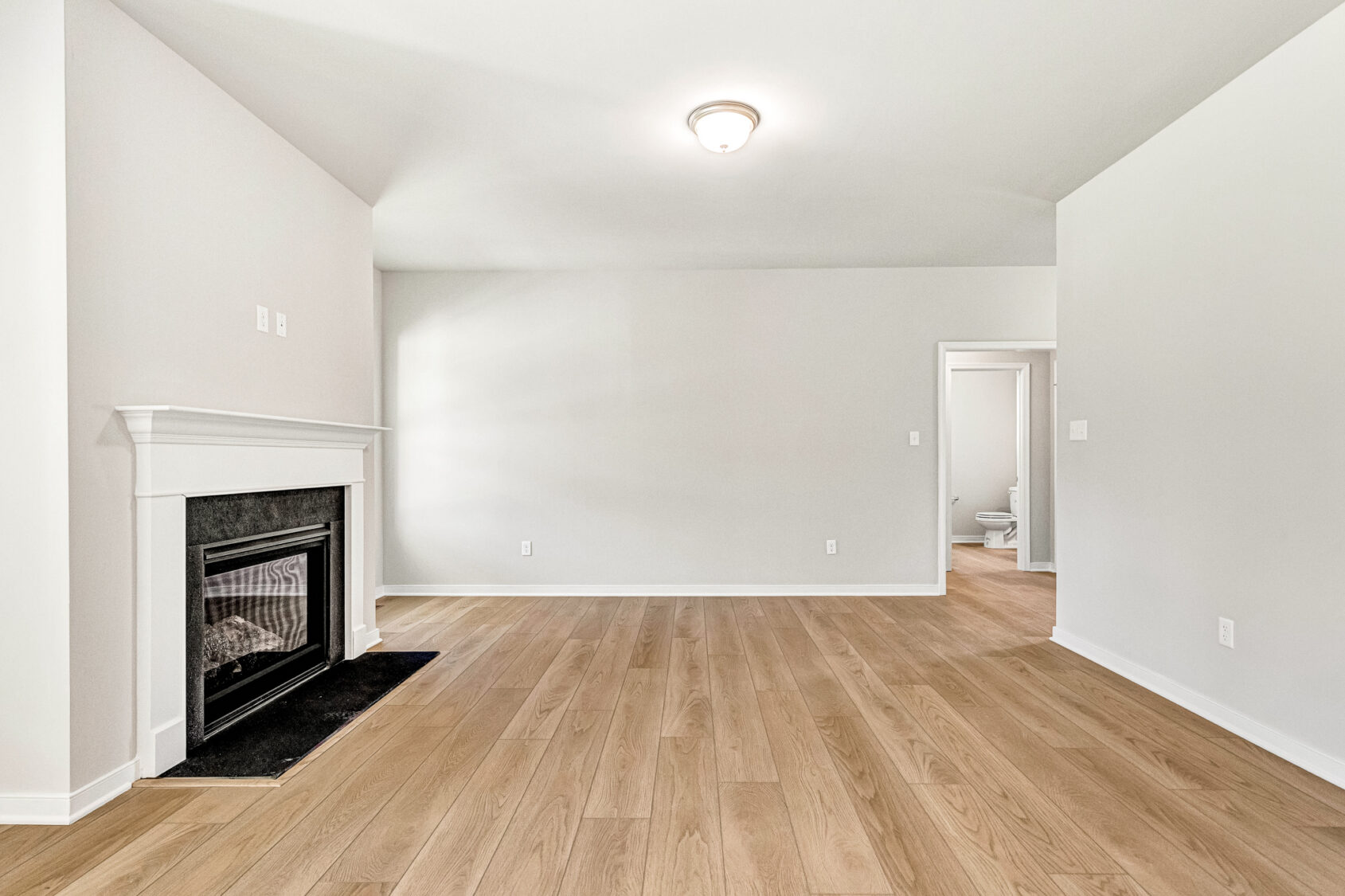 Empty living room with light wood floors in Poplar Village, featuring a fireplace and a doorway to the bathroom.