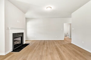 Empty living room with light wood floors in Poplar Village, featuring a fireplace and a doorway to the bathroom.