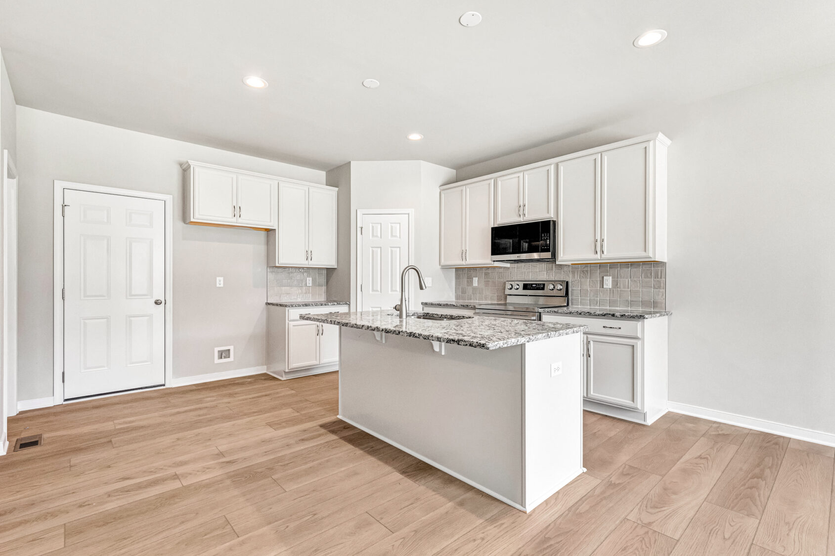 Bright modern kitchen in Poplar Village with white cabinets, granite countertops, an island, and light wood flooring.