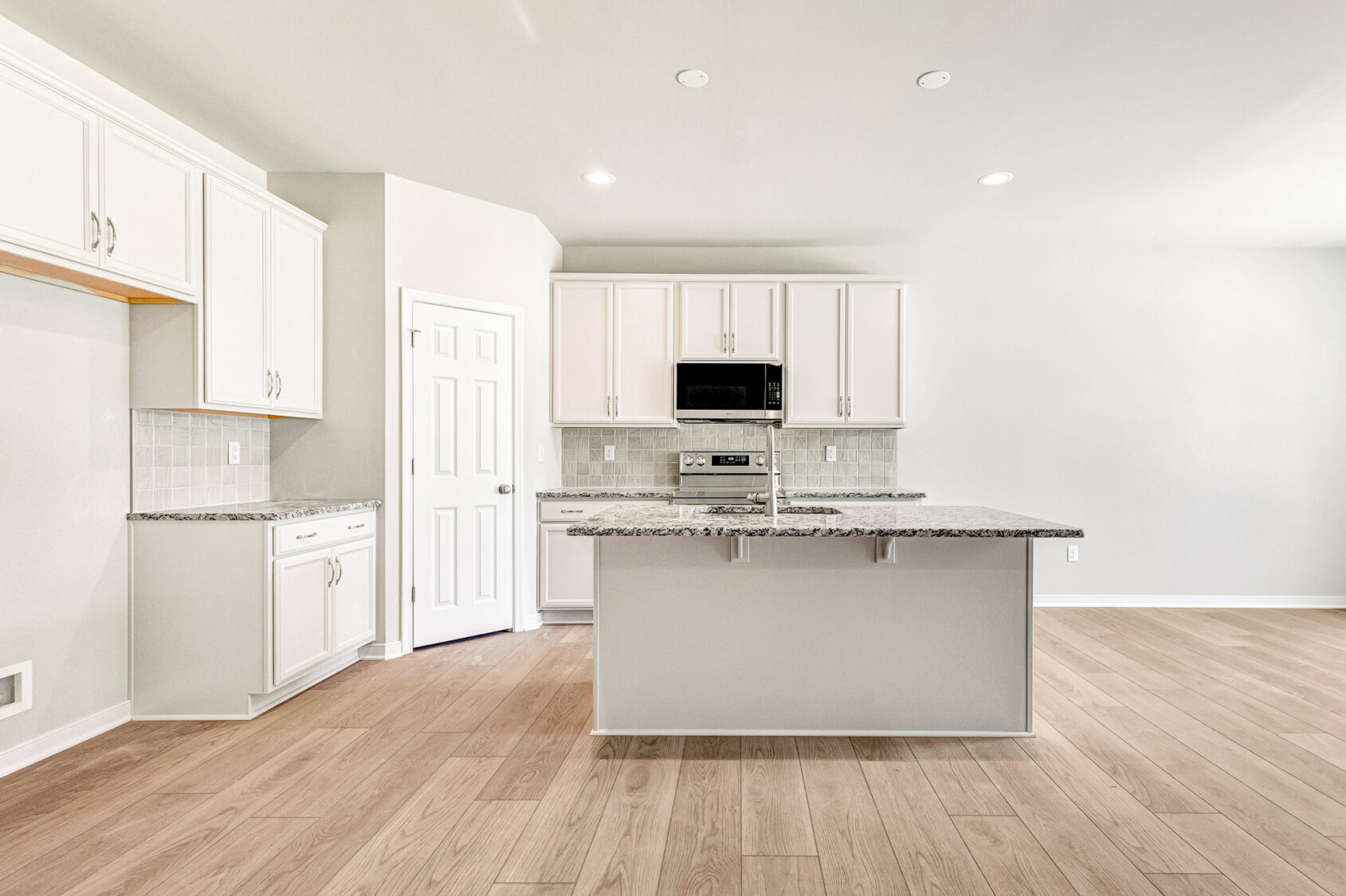 Modern kitchen in Poplar Village with white cabinets, granite countertops, island, wood floors, and built-in microwave.