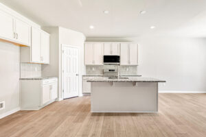 Modern kitchen in Poplar Village with white cabinets, granite countertops, island, wood floors, and built-in microwave.