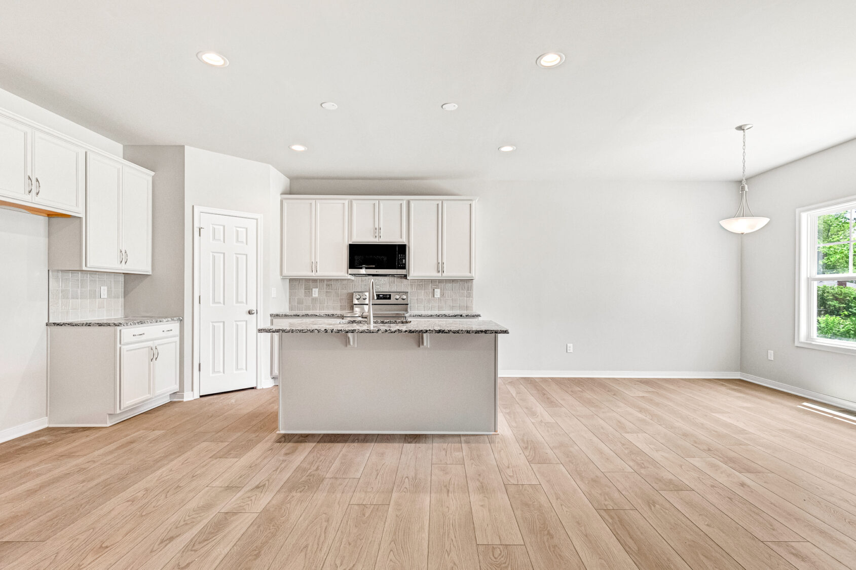 Bright modern kitchen in Poplar Village with white cabinets, granite island, wood floors, and natural light.