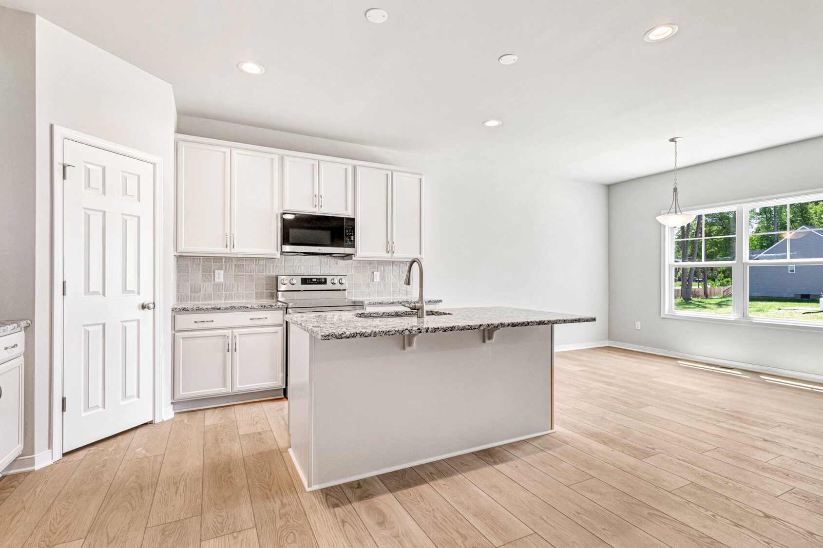 Bright modern kitchen at Poplar Village Lot 26 with white cabinets, island, granite counters, wood floors, and large windows.