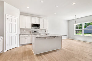 Bright modern kitchen at Poplar Village Lot 26 with white cabinets, island, granite counters, wood floors, and large windows.