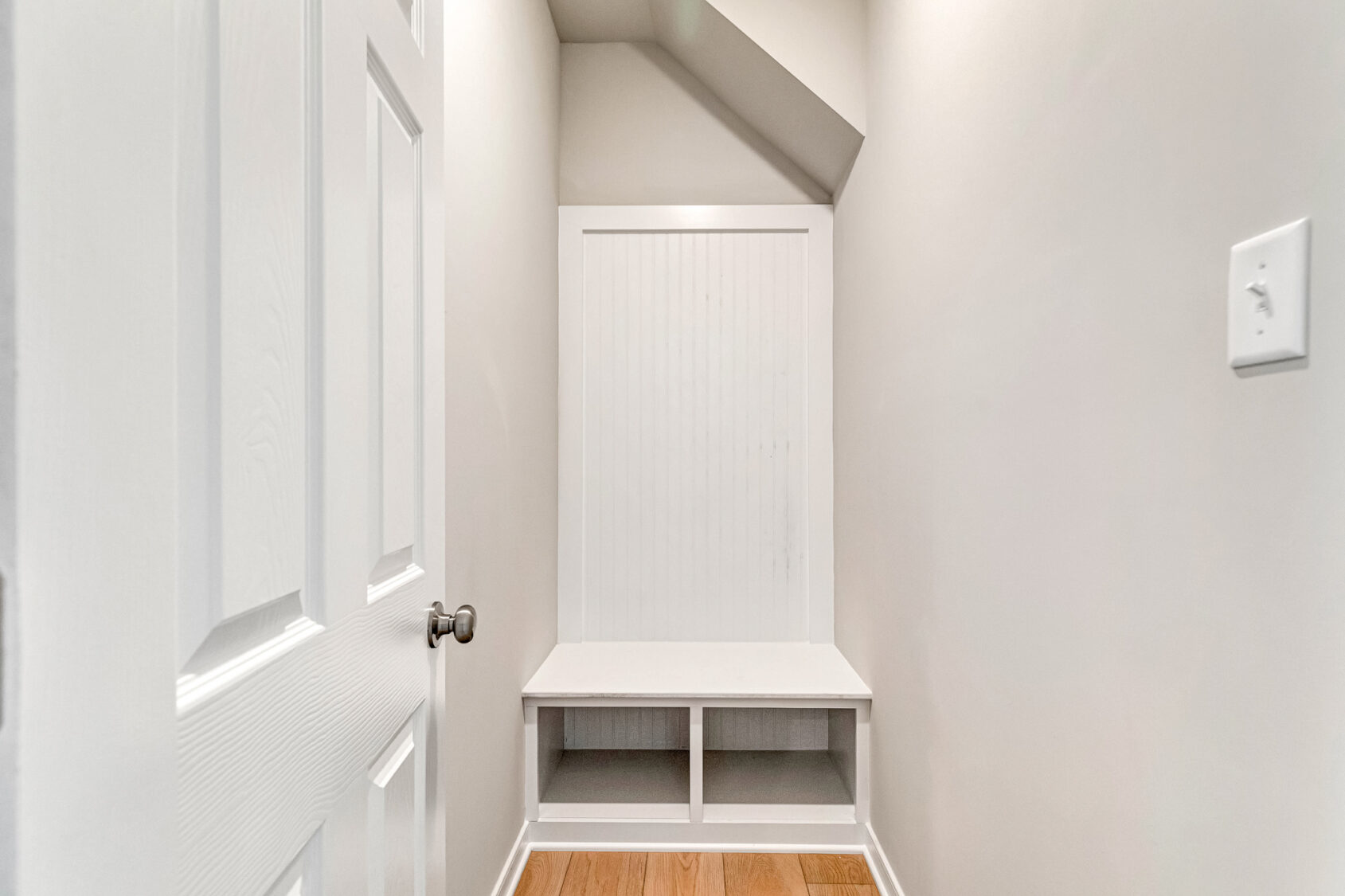 White built-in bench with cubbies beneath and paneled back, set in a Poplar Village Lot 26 nook with light walls.