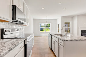 Bright modern kitchen in Poplar Village with white cabinets, stainless appliances, and a granite island facing a sunny window.