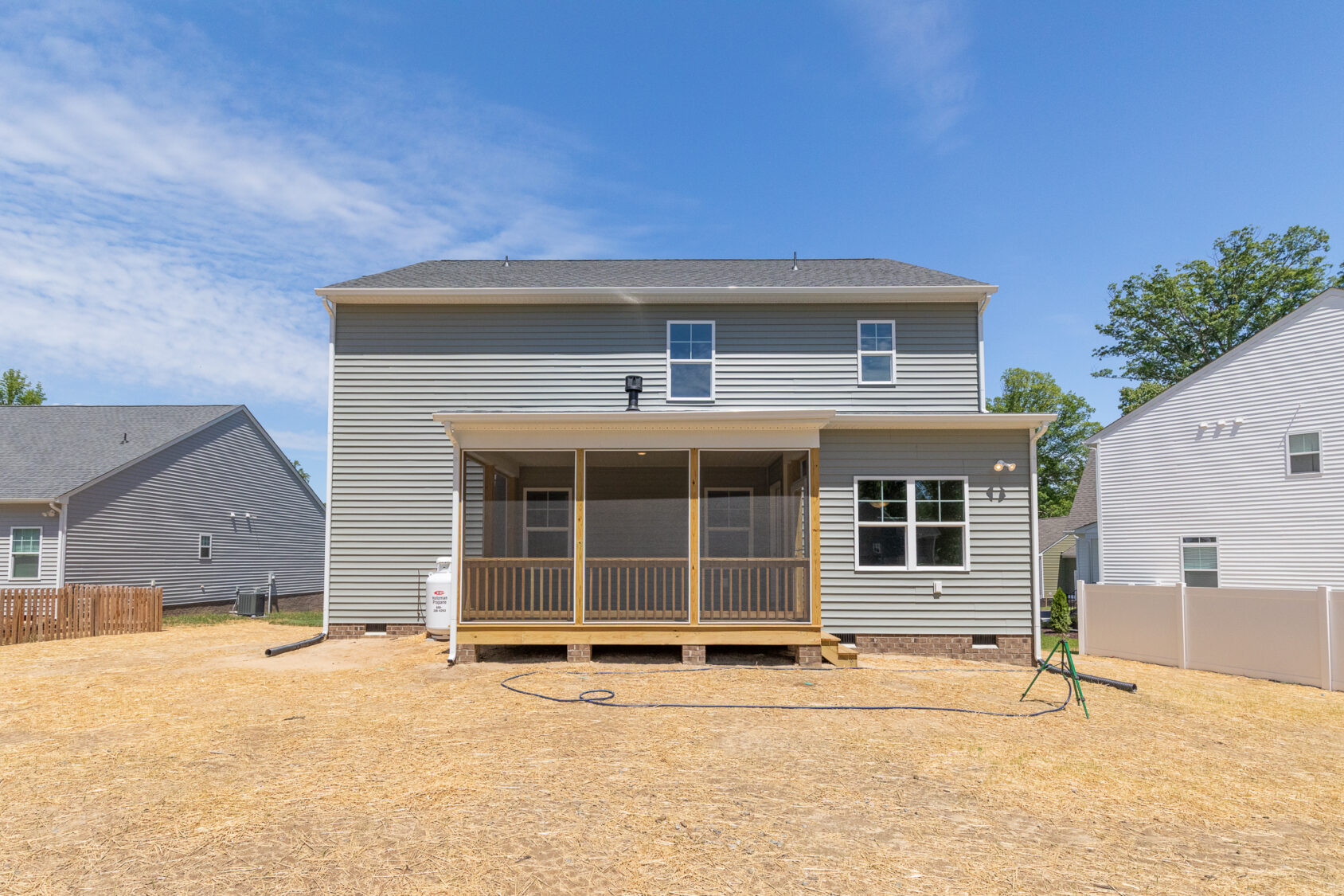 Two-story gray house in Poplar Village with a screened porch and dry, straw-covered backyard under a clear blue sky.