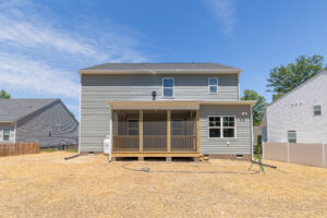 Two-story gray house in Poplar Village with a screened porch and dry, straw-covered backyard under a clear blue sky.