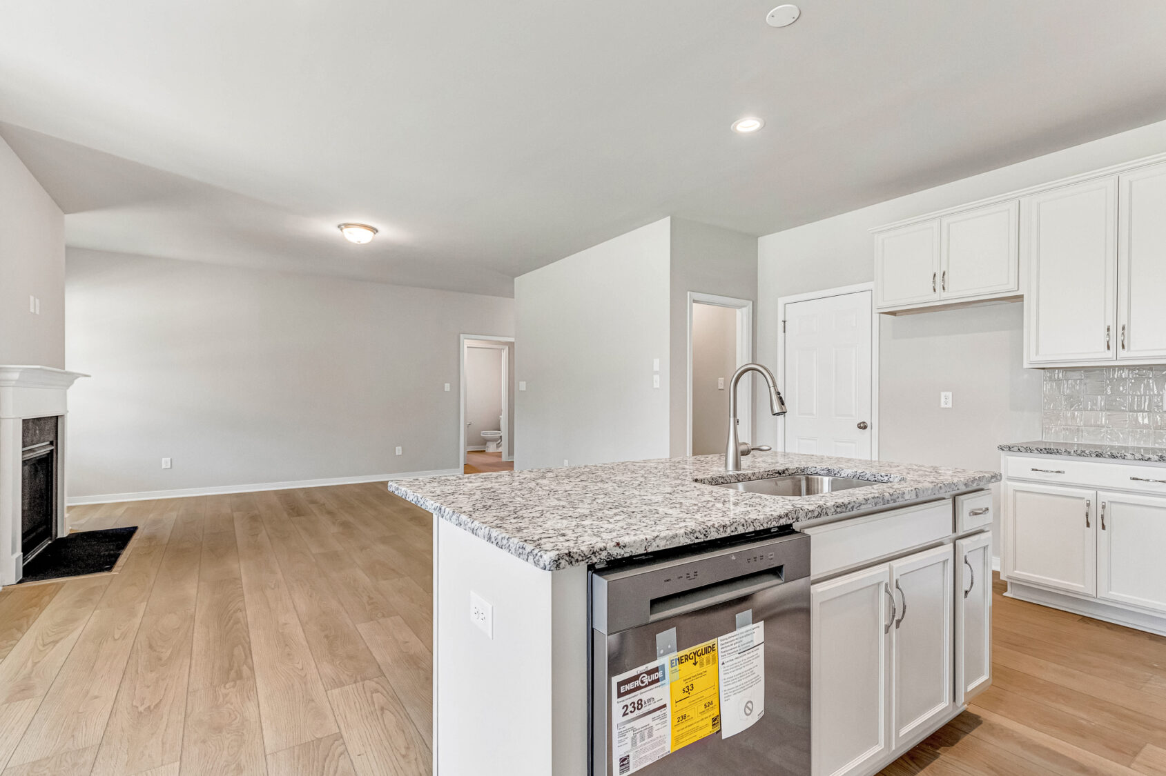 Modern kitchen at Lot 26, Poplar Village features granite island, white cabinets, and open living with wood floors.