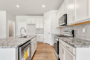 Modern kitchen in Poplar Village with white cabinets, granite countertops, stainless steel appliances, and wood flooring.