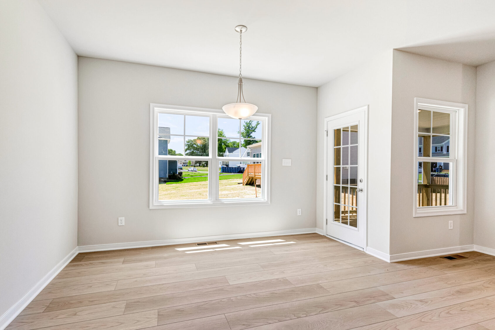 Bright, empty room in Poplar Village Lot 26 with light wood floors, large window, glass door, and white walls.
