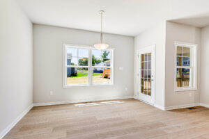 Bright, empty room in Poplar Village Lot 26 with light wood floors, large window, glass door, and white walls.