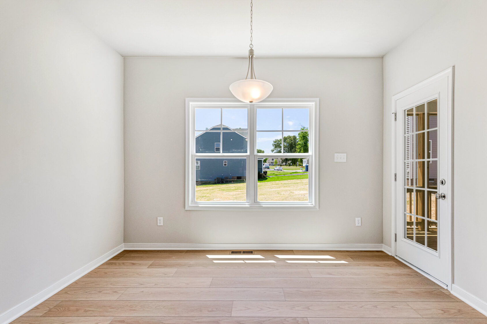 Bright, empty room in Poplar Village with light wood floors, a hanging light, window, and glass door to the outside.