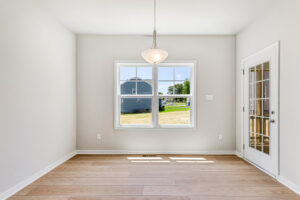 Bright, empty room in Poplar Village with light wood floors, a hanging light, window, and glass door to the outside.