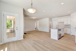 Bright, modern open-plan kitchen and living area with light wood floors and large windows in Poplar Village Lot 26.
