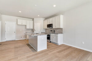 Modern kitchen in Lot 26 with white cabinets, stainless steel appliances, and a center island on light wood floors.