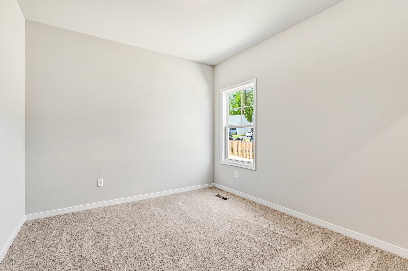 Empty room in Poplar Village, Lot 26, with beige carpet, white walls, and natural light from a single window.